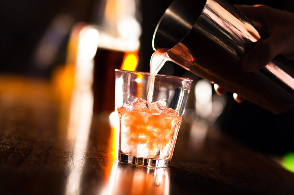 Hands of a bartender pouring a drink into a glass