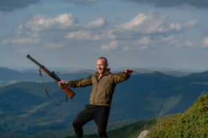 Hunting - Men hobby. Excited Hunter with Powerful Rifle with Scope Spotting Animals. Male with a gun. A hunter with a hunting gun hunt in summer forest