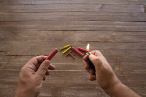 Image of the hands of a man who lights the fuse of a firecracker with a lighter. Reference you have celebrations and the danger of the barrels