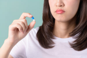 Forget taking medicine. Confused woman holds head and looks at pills on green background. Asian woman forget to take medicine, miss medication dose, and think of next prescription with a pill in hand.