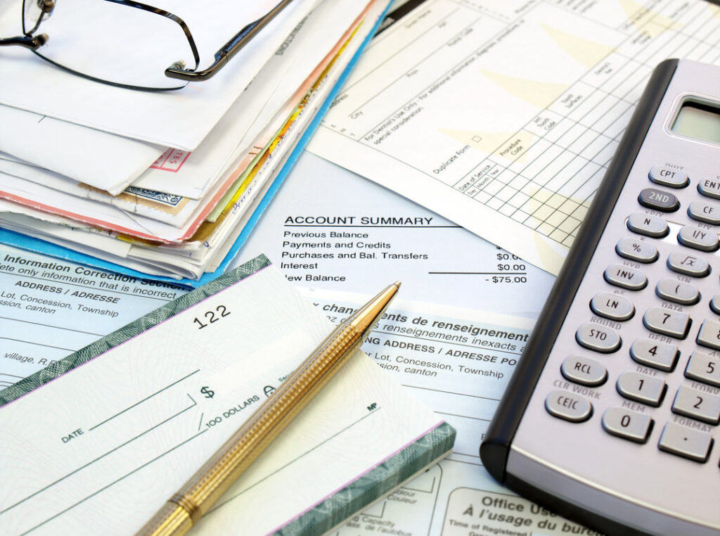 A pile of bills, checkbook, pen and calculator on the table.