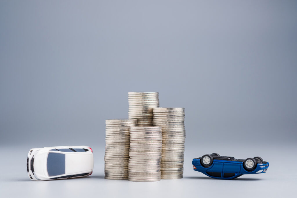 Stacks of money coins with a model of two toy cars after collision, car accident and insurance