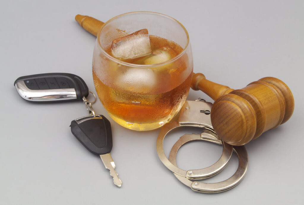 Drunk driving and court concept. Judge gavel, handcuffs, car key with glass of whisky on gray background.